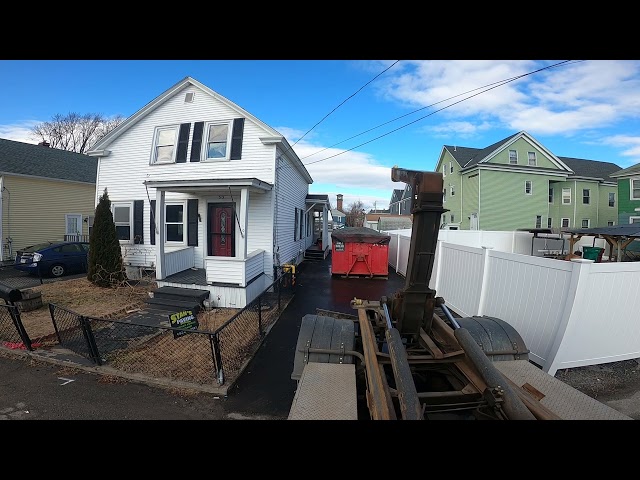 hooklift truck in tiny driveway picking up dumpster