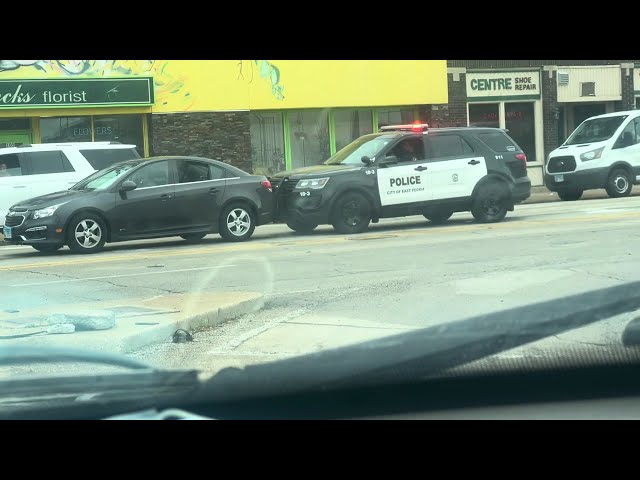 Law enforcement officer uses the police cruiser to push a broke down car out of the inters